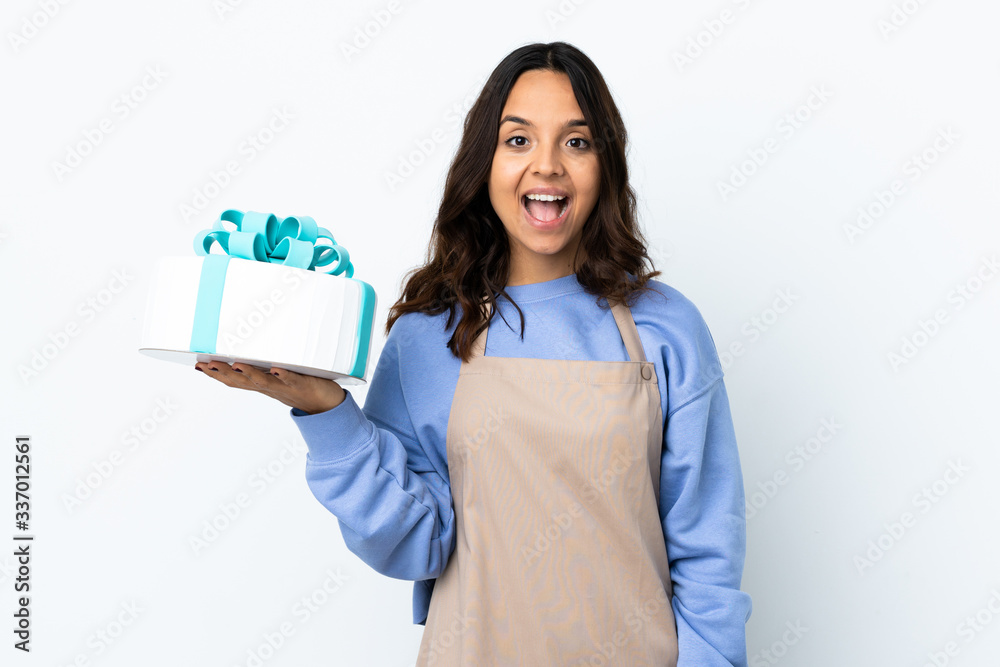 Pastry chef holding a big cake over isolated white background with surprise facial expression Pastry chef holding a big cake over isolated white background with surprise facial expression
