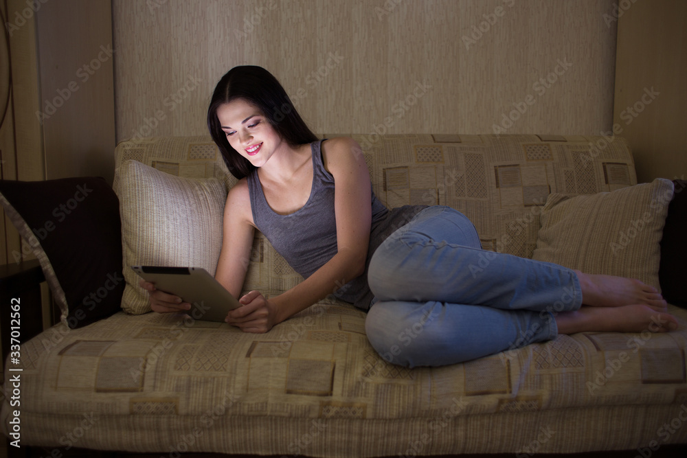 Smiling girl looking at the tablet in the dark at night Smiling girl looking at the tablet in the dark at night