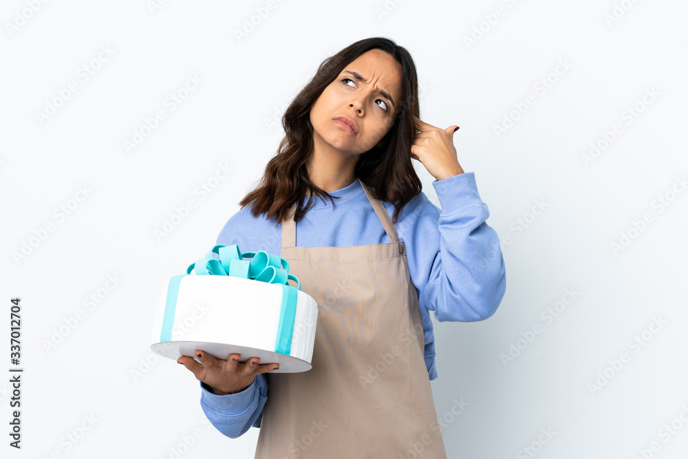Pastry chef holding a big cake over isolated white background making the gesture of madness putting finger on the head Pastry chef holding a big cake over isolated white background making the gesture of madness putting finger on the head