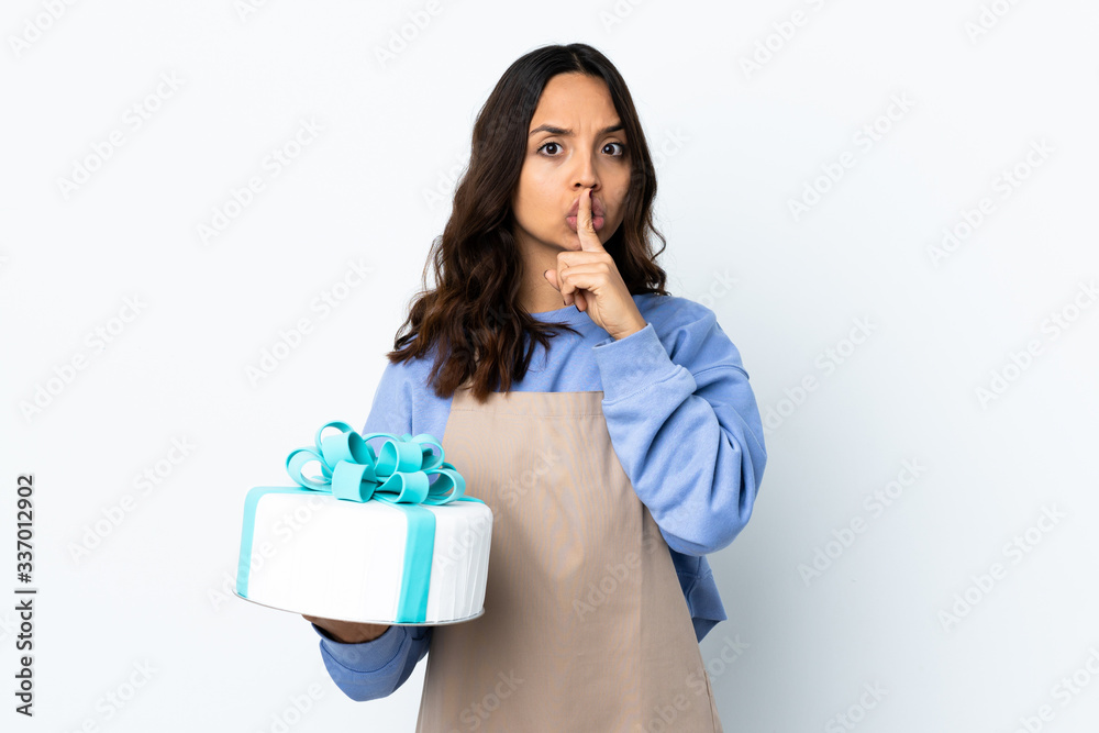 Pastry chef holding a big cake over isolated white background pointing to the side and doing silence gesture Pastry chef holding a big cake over isolated white background pointing to the side and doing silence gesture