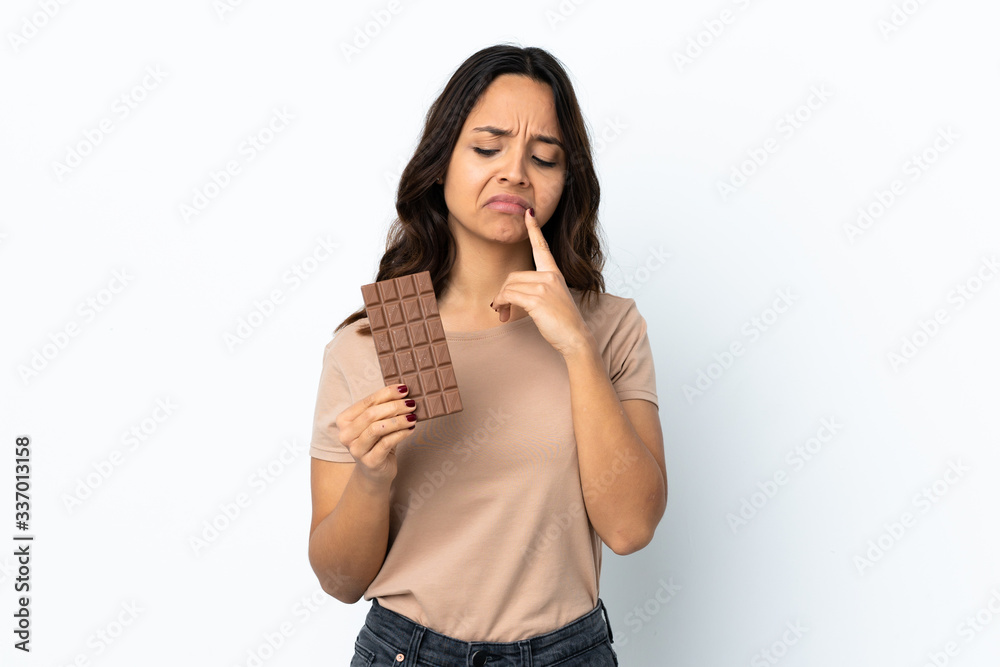 Young woman over isolated white background taking a chocolate tablet and having doubts Young woman over isolated white background taking a chocolate tablet and having doubts