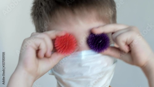 On a white background, a masked boy with brown hair puts balls similar to coronavirus instead of eyes and smiles at the camera close-up, balls of purple and pink color photo