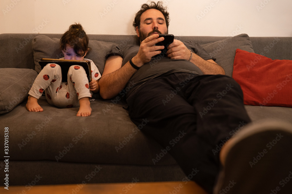 father and daughter with pacifiers on the sofa while using a tablet and a phone during quarantine father and daughter with pacifiers on the sofa while using a tablet and a phone during quarantine