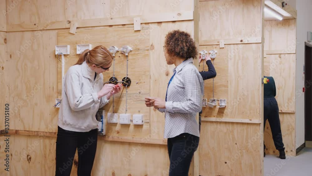 Dolly shot of female tutor with trainee electricians in workshop studying for apprenticeship at college - shot in slow motion