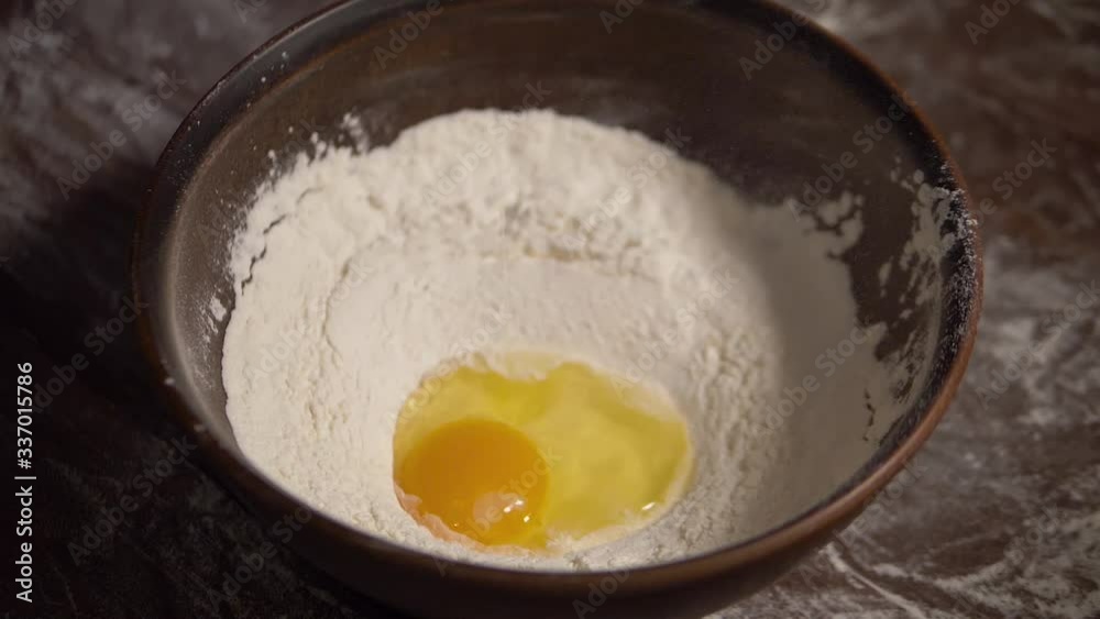Slow motion of falling egg into flour. Egg dropping into flour poured into a brown bowl, closeup slow motion. Egg yolk falls into the flour. Rustic style. Food blog. Preparation of dough, slow motion Slow motion of falling egg into flour. Egg dropping into flour poured into a brown bowl, closeup slow motion. Egg yolk falls into the flour. Rustic style. Food blog. Preparation of dough, slow motion