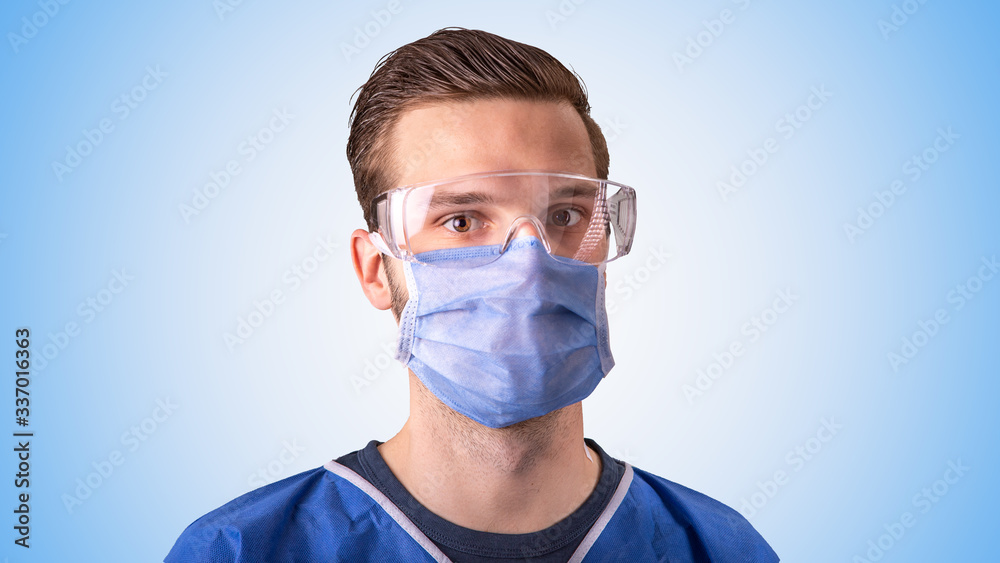 Arzt oder Pfleger mit Mundschutz und Schutzbrille vor hellblauem Hintergrund Arzt oder Pfleger mit Mundschutz und Schutzbrille vor hellblauem Hintergrund
