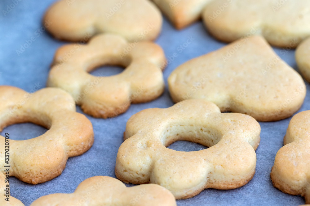 Baked shortbread cookies in the form of flowers and hearts on a baking sheet with parchment paper just taken out of the oven. Tea snack for breakfast. Selective focus. Closeup view
