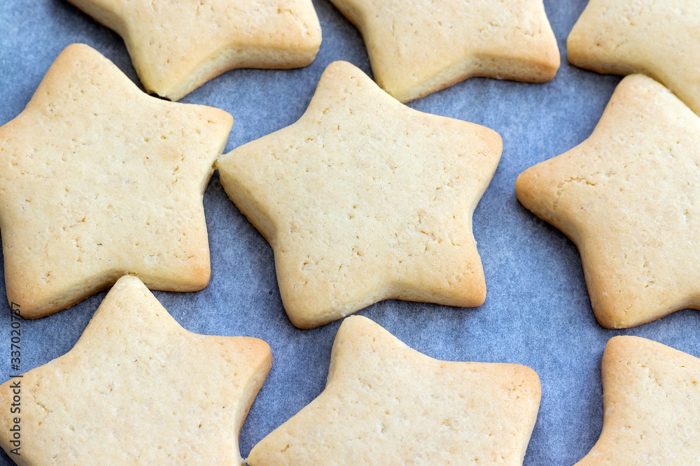 Baked shortbread cookies in the form of stars on a baking sheet with parchment paper just taken out of the oven. Tea snack for breakfast. Selective focus. Closeup top view Baked shortbread cookies in the form of stars on a baking sheet with parchment paper just taken out of the oven. Tea snack for breakfast. Selective focus. Closeup top view
