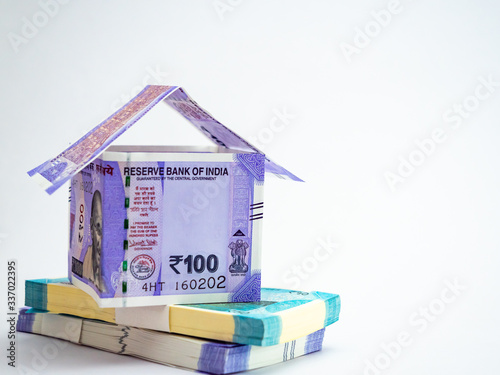 A house made with folded notes and bundles of money on white surface for finance concept.