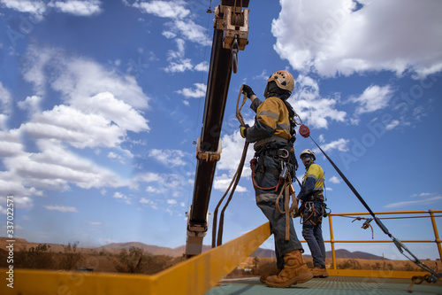 Safe workplace rigger wearing working at heights harness having clipping an inertia reel shock absorbing hook fall arrest device on the back safety harness hook while working from exposure open edges 