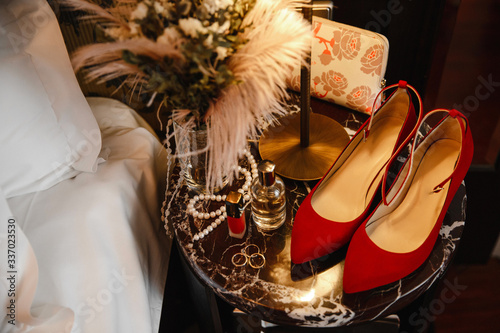 The red wedding. Wedding rings on a white and red invitation next to a perfume bottle, red wedding shoes and flowers