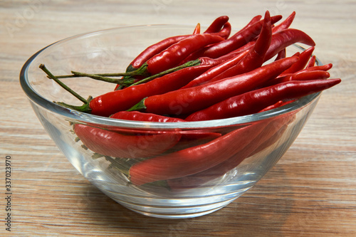 glass cup with pods of red hot pepper on a wooden table surface close-up