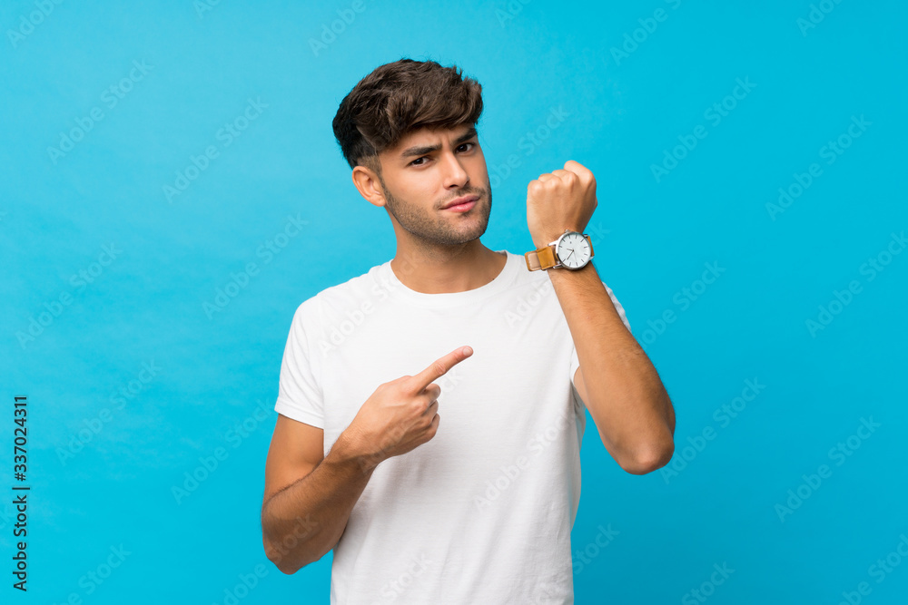 Young handsome man over isolated blue background showing the hand watch with serious expression serious because it is getting late