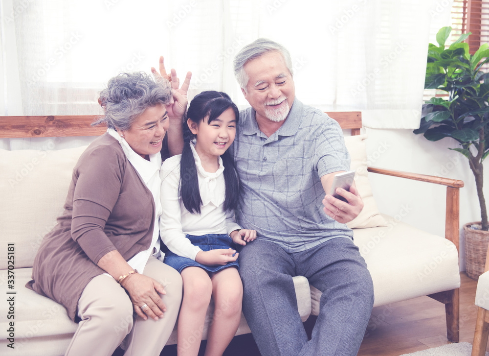 Asian Grandfather taking selfie with couple Grandparent and granddaughter with happy feeling by mobile phone in house, Long live and Elderly society, Warm family and stay at home,leisure life concept. Asian Grandfather taking selfie with couple Grandparent and granddaughter with happy feeling by mobile phone in house, Long live and Elderly society, Warm family and stay at home,leisure life concept.