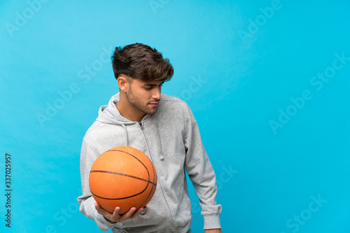 Young handsome man over isolated blue background with ball of basketball © luismolinero