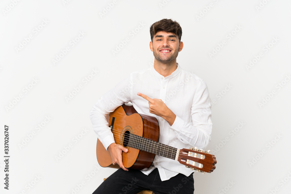Young handsome man with guitar over isolated white background pointing to the side to present a product Young handsome man with guitar over isolated white background pointing to the side to present a product