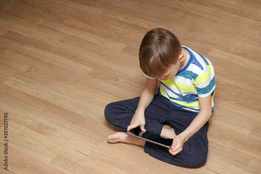 Modern generation. The child plays games or watches cartoons. A boy is playing with his tablet. - obrazy, fototapety, plakaty 