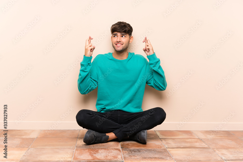 Young handsome man sitting on the floor with fingers crossing Young handsome man sitting on the floor with fingers crossing