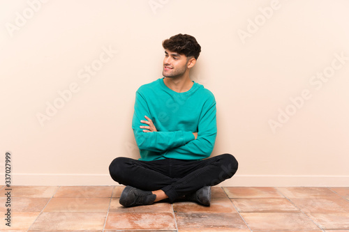Young handsome man sitting on the floor looking to the side