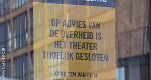 silhouette in glass reflection reads announcement on glass entrance door of a theatre, in Dutch meaning: shut down until further notice due to coronavirus