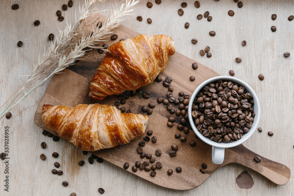Cup full of coffee beans, two croissants and spica on wooden board
