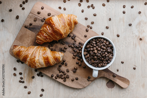 Cup full of coffee beans and two croissants on wooden board