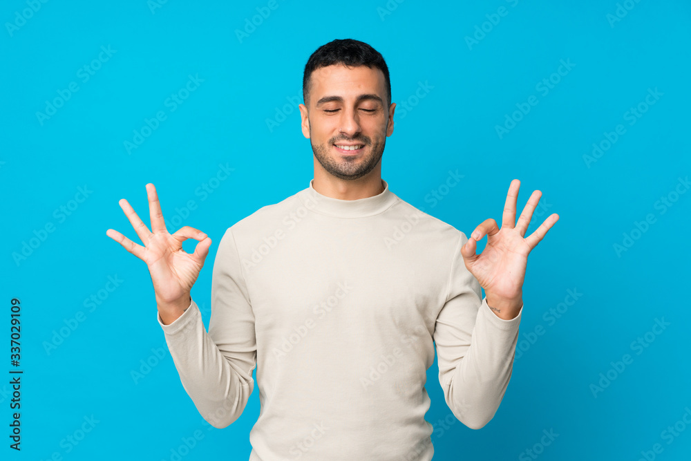 Naklejka premium Young man over isolated blue background in zen pose