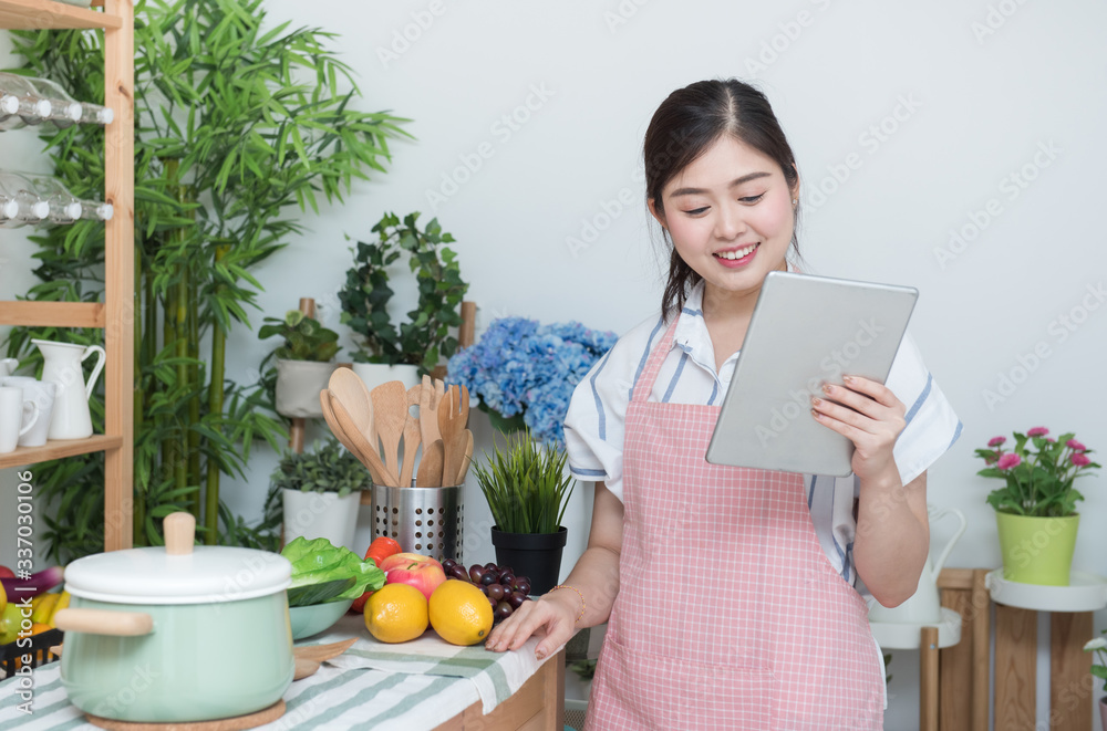 Φωτογραφία Happy asian woman looking recipe tablet kitchen reading cooking at home,University colleague student study online with social media,Social distancing, stay at home and work from home concept