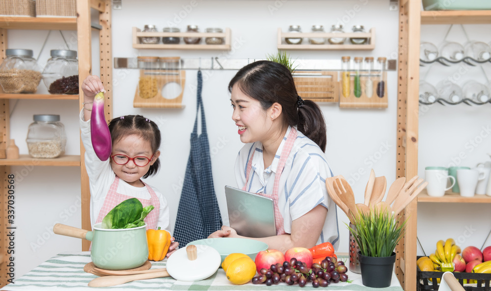 Φωτογραφία Asian woman mother and daughter play together in kitchen,mom hold tablet for teach little girl how to cook in semester break,social distancing, stay home concept