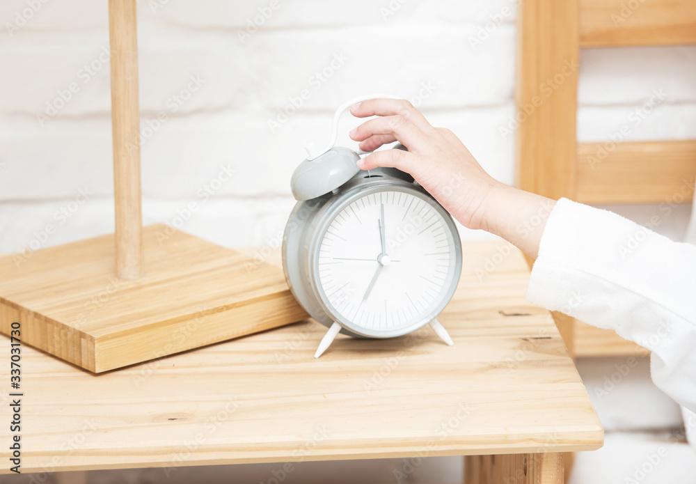 Φωτογραφία Hand of little asian girl touch alarm clock while she laying on white bed lazy to wake up and put clock stop ringing