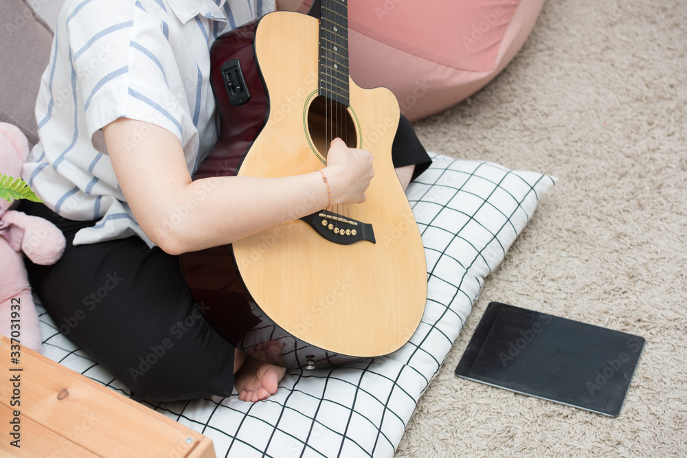 Φωτογραφία Asian woman playing records on guitar supported by tablet digital computer, female teacher teaching musical online at homework from home and social distancing concept