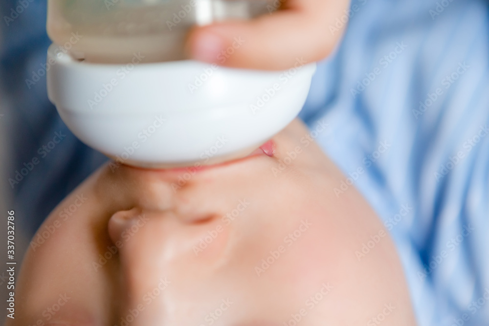 Naklejka premium Baby boy brunette lies on the bed in blue pajamas and drinks milk from a bottle. Baby food