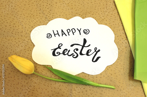 Photo of white paper in the shape of cloud on beige fabric. Happy Easter - hand written lettering. Color abstract mockup template with flower tulip