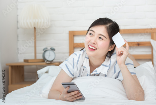 Portrait of young asian woman lying on bed using digital smart mobile phone for shopping online with credit card payment.
