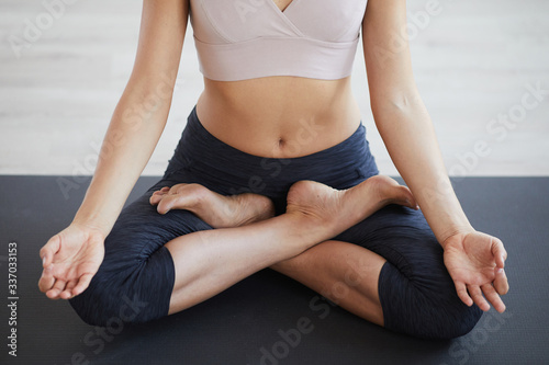 Close-up of young slim woman in sport bra sitting on exercise mat in lotus position