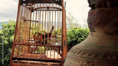 Bird encased in a cage next to the old bell photo