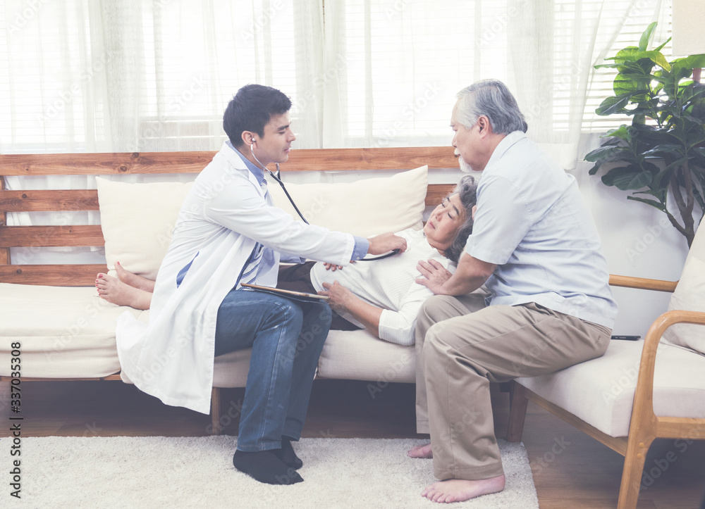 Caucasian doctor use tablet and talk with old asian female patient while lay down on sofa about disease symptom, elderly health check up at home. Caucasian doctor use tablet and talk with old asian female patient while lay down on sofa about disease symptom, elderly health check up at home.