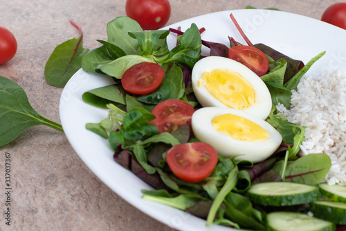 Salad of green vegetables, tomato and rice in a white plate. Rice with vegetables and eggs on a white plate.