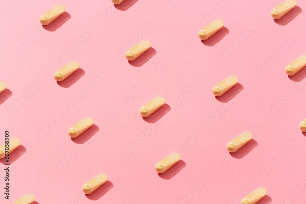 Yellow medicine pills flat laid inside the pattern, on top of colorful pink background.