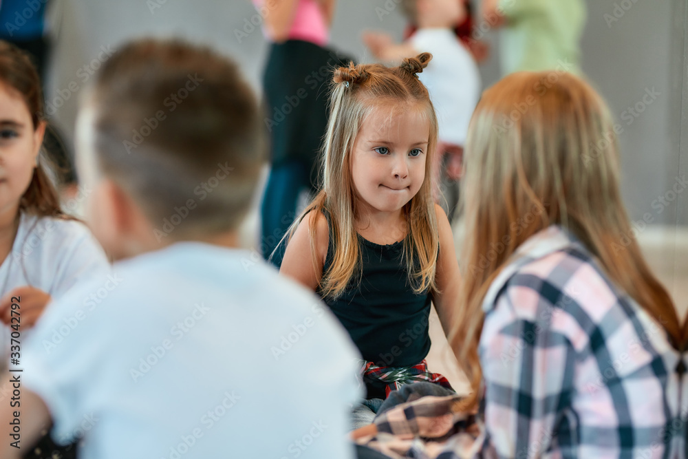 Fototapeta premium Portrait of children talking with each other while sitting on the floor and having a break in the dance studio