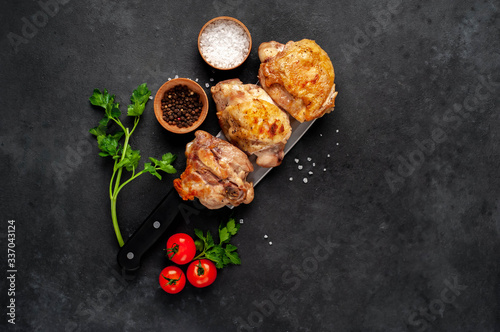 Grilled chicken thighs on a knife with spices on a stone background with copy space for your text