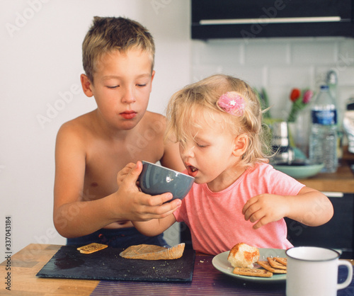 Canvas Print Elder brother taking care of junior sister and helping her drink from the cup during breakfast