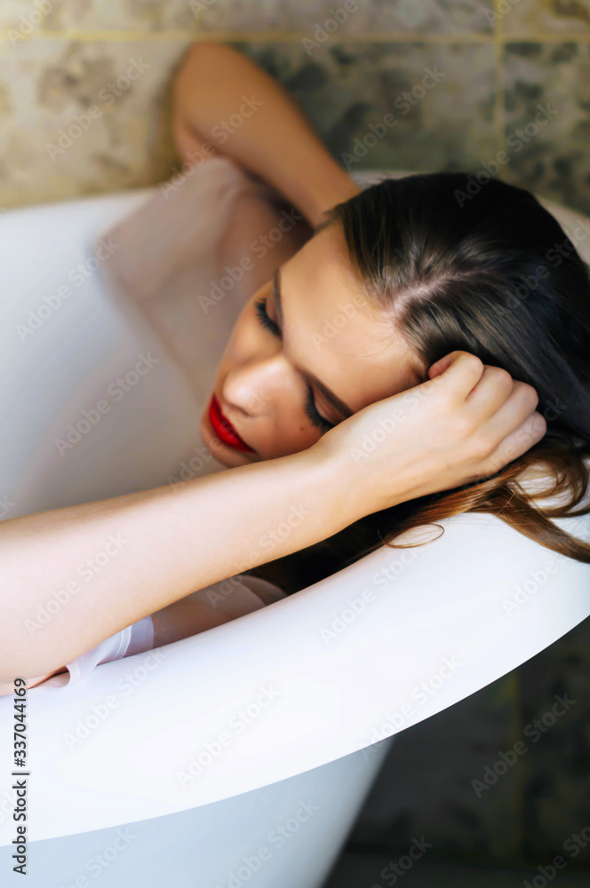 Obraz premium Beautiful blonde girl with red lipstick is lying in the bathroom holding her head with her hands. Fashion, beauty, book cover.
