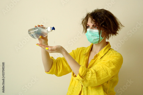 Young caucasian woman in medical mask washing hands with sanitizer. Girls wearing yellow shirt and manicure