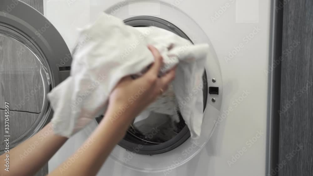 Female hand takes white clothes from laundry machine. Loading washing machine. Load clothes to washer machine. Load clothes laundry washing machine. Preparing laundry washing Female hand takes white clothes from laundry machine. Loading washing machine. Load clothes to washer machine. Load clothes laundry washing machine. Preparing laundry washing