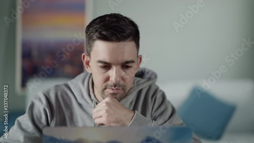 Work from home. A young white male is concentrating on the laptop and thoughtfully touches his chin