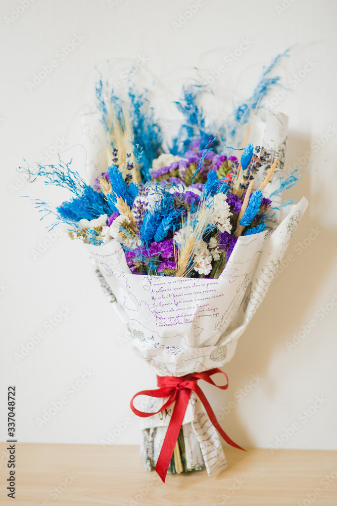 Bouquet of dried flowers in blue and purple tones with red ribbon. Dried flowers of cotton, wheat, lavender, statice (kermek), munni and others. Flower composition. Bouquet of dried flowers in blue and purple tones with red ribbon. Dried flowers of cotton, wheat, lavender, statice (kermek), munni and others. Flower composition.