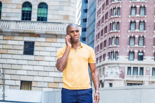 Young African American Man Street Fashion in New York City. Wearing yellow short sleeve shirt, young black college student with short hair, standing outside office building, talking on cell phone...