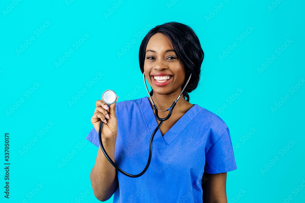 Portrait of a happy and smiling female doctor or nurse wearing blue scrubs uniform holding stethoscope, isolated on blue background Portrait of a happy and smiling female doctor or nurse wearing blue scrubs uniform holding stethoscope, isolated on blue background