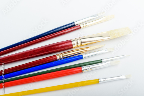 Many professional artist paintbrushes displayed horizontally isolated on a white studio paper, photographed with soft focus 